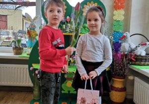 Widok na chłopca wręczającego dziewczynce tulipana i torebkę z prezentem.